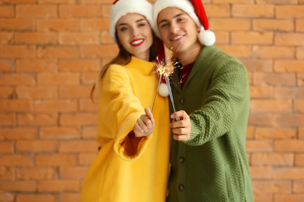 Ευτυχισμένο νεαρό ζευγάρι με χριστουγεννιάτικα βεγγαλικά σε φόντο τούβλων — Φωτογραφία Αρχείου