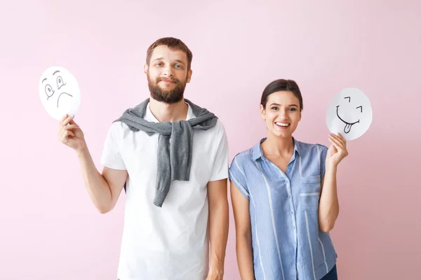 Pareja feliz sosteniendo hojas de papel con emoticonos dibujados sobre fondo de color — Foto de Stock