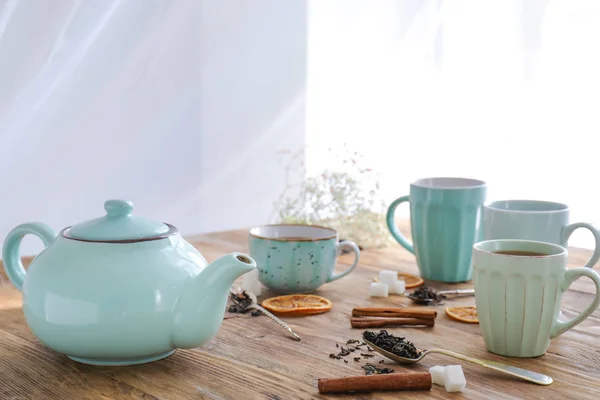 Cups and teapot with hot beverage on wooden table — Stock Photo, Image