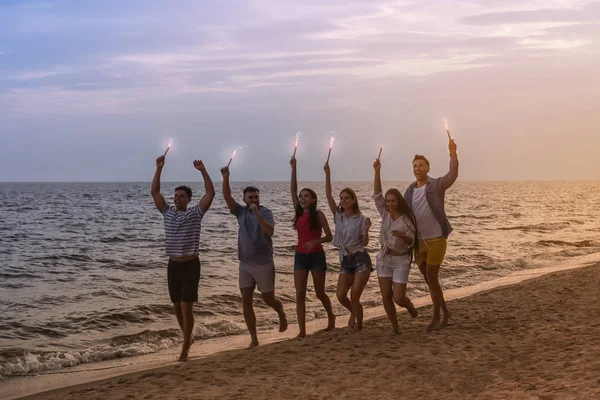 Happy friends with sparklers on sea beach at resort — Stock Photo, Image