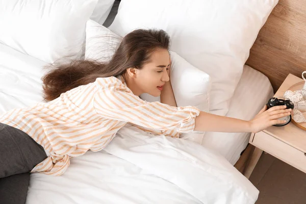 Morning of beautiful young woman turning off alarm clock while lying in bed — Stock Photo, Image