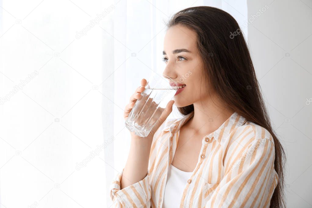 Morning of beautiful young woman drinking water near window