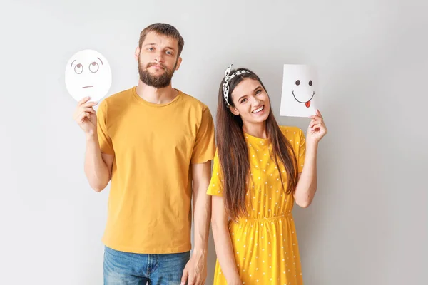 Casal feliz segurando folhas de papel com emoticons desenhados em fundo cinza — Fotografia de Stock