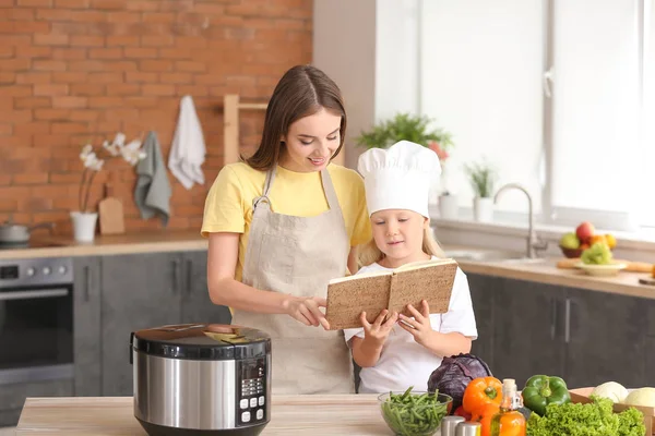 Woman and her little daughter with recipe book and modern multi cooker in kitchen — Stock Photo, Image