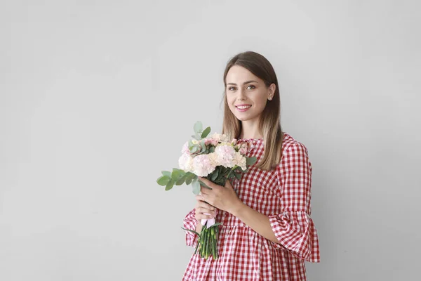 Beautiful young woman with bouquet of carnation flowers on light background — Stock Photo, Image