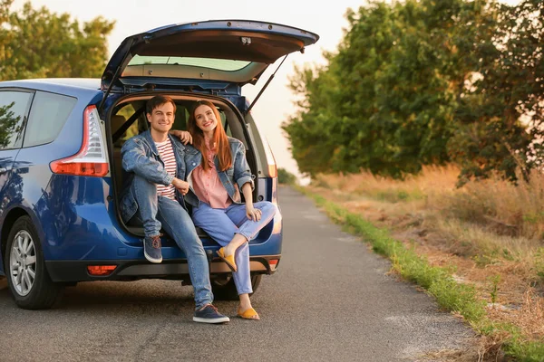 Happy couple sitting in trunk of their new car in countryside — Stock Photo, Image