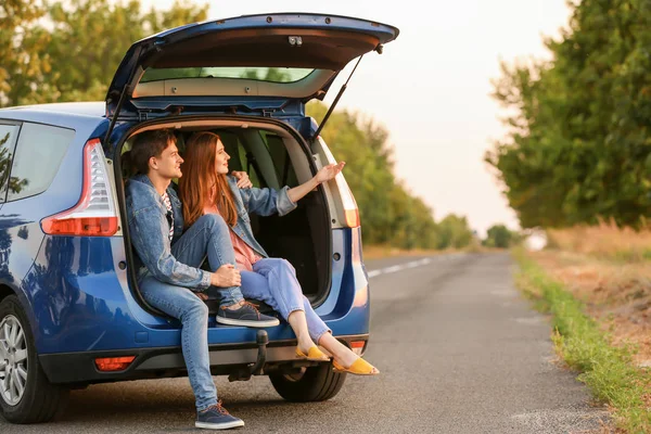 Happy couple sitting in trunk of their new car in countryside — Stock Photo, Image