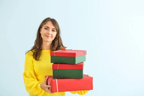 Happy young woman with Christmas gifts on light background — Stock Photo, Image