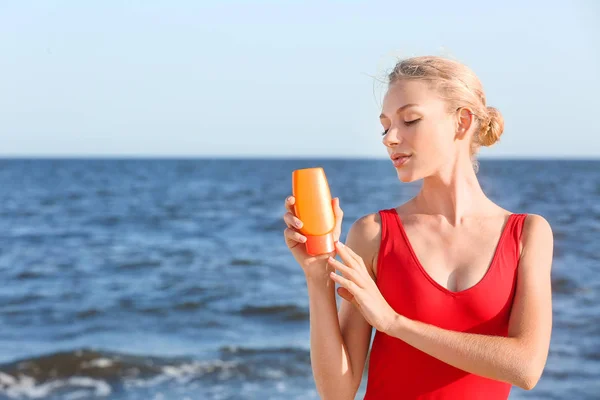 Mooie jonge vrouw met zon bescherming crème op zee strand — Stockfoto