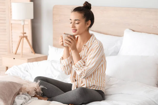 Morning of beautiful young woman drinking coffee while sitting on bed — Stock Photo, Image