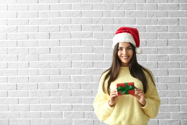 Vacker ung kvinna med julklapp mot tegelvägg — Stockfoto