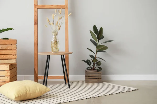 Mesa con alfombra, almohada, planta y escalera cerca de pared de luz en la habitación —  Fotos de Stock