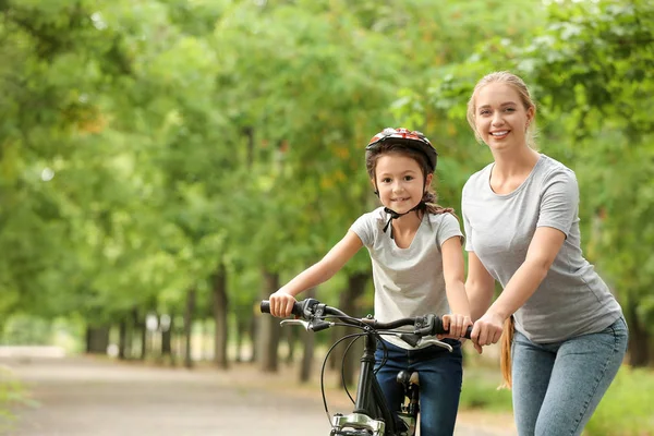 Mother teaching her daughter to ride bicycle outdoors — Stock Photo, Image