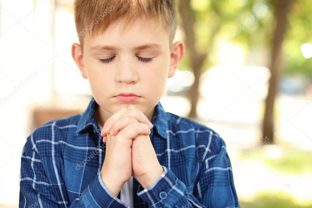 Cute little boy praying outdoors