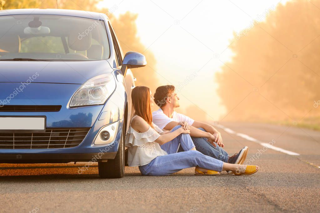 Happy couple near their new car sitting on road in countryside