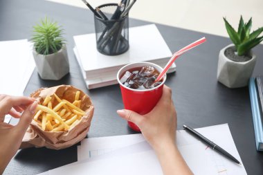 Kadın soğuk kola içiyor ve ofiste masada patates kızartması yiyor