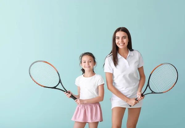 Mała dziewczynka i jej matka z rakietami tenisowym na kolorowym tle — Zdjęcie stockowe