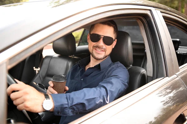Successful businessman drinking coffee while driving modern car — Stock Photo, Image