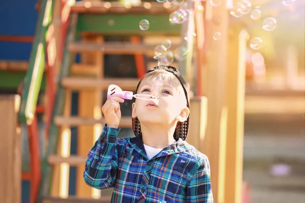 Netter kleiner Junge pustet Seifenblasen auf Spielplatz — Stockfoto