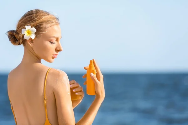 Mooie jonge vrouw met zon bescherming crème op zee strand — Stockfoto