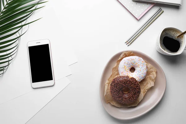 Leckere Donuts mit Handy, Tasse Kaffee und Schreibwaren auf weißem Hintergrund — Stockfoto