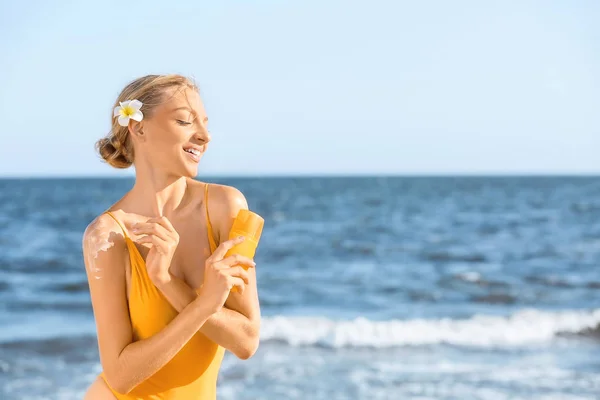 Hermosa mujer joven con crema de protección solar en la playa de mar — Foto de Stock