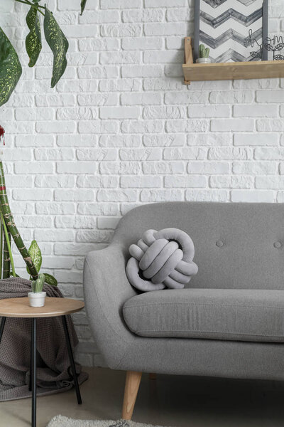 Soft couch with stylish pillow near white brick wall in room