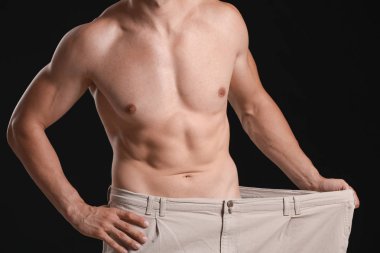 Koyu arka planda gevşek pantolon yakışıklı kaslı adam. Kilo kaybı kavramı