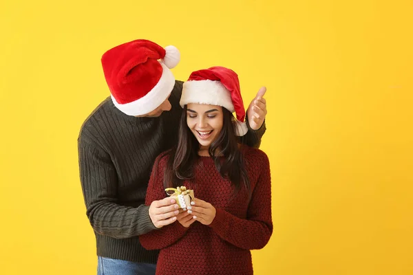 Man giving his girlfriend Christmas present against color background — Stock Photo, Image