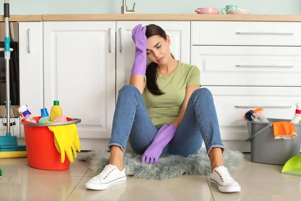 Уставшая молодая женщина, сидящая на полу после уборки кухни — стоковое фото