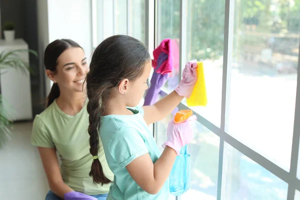 Woman and her little daughter cleaning window in flat — Stock Photo, Image