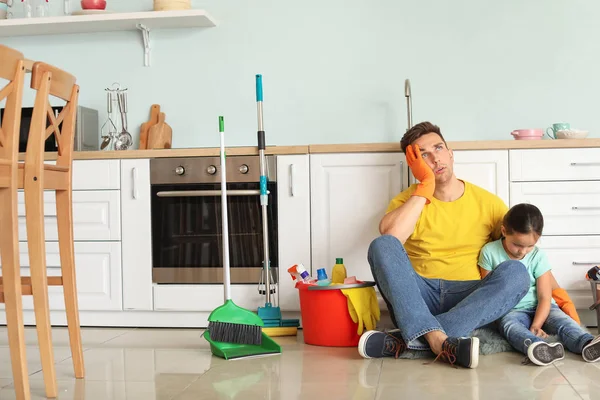 Zmęczony mężczyzna i jego mała córka siedzi na podłodze po sprzątanie kuchni — Zdjęcie stockowe