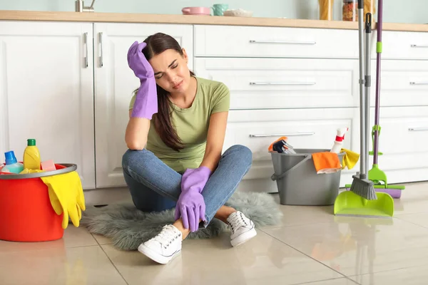 Trött ung kvinna sitter på golvet efter rengöring kök — Stockfoto