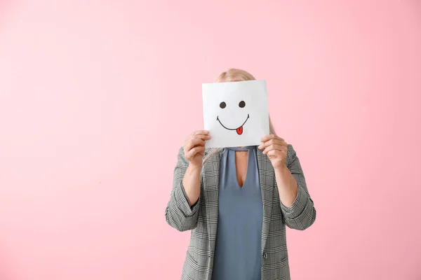 Mogen kvinna gömmer ansiktet bakom uttryckssymbol mot färg bakgrund — Stockfoto
