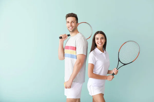 Young couple with tennis rackets on color background — Stock Photo, Image