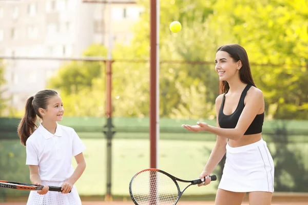 Liten flicka och hennes mamma spelar tennis på planen — Stockfoto