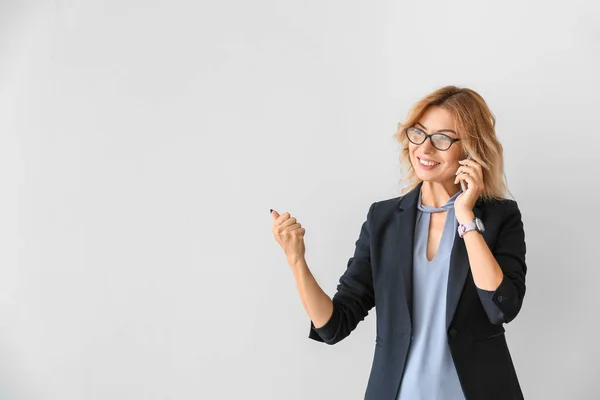 Portrait of beautiful businesswoman talking by phone on light background — Stock Photo, Image