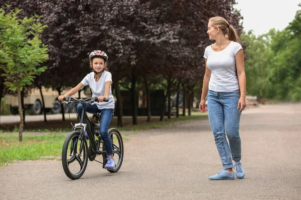 Mother teaching her daughter to ride bicycle outdoors — Stock Photo, Image