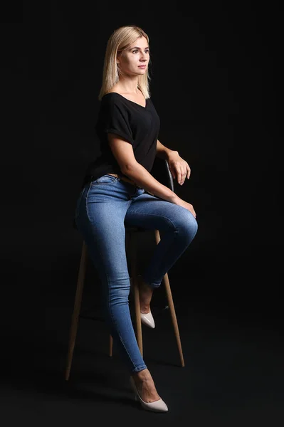 Beautiful stylish woman sitting on chair against dark background — Stock Photo, Image