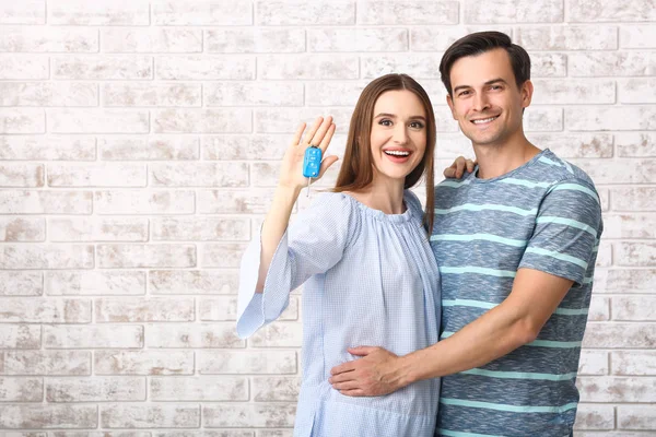 Happy couple with key from their new car on brick background — Stock Photo, Image