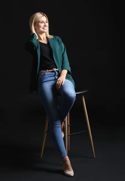 Beautiful stylish businesswoman sitting on chair against dark background — Stock Photo, Image