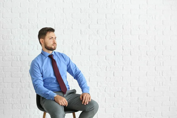 Portrait of stylish businessman sitting on chair against white brick wall — Stock Photo, Image