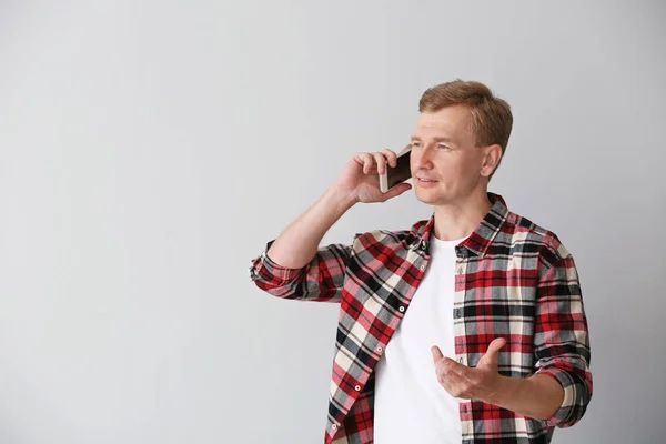 Portrait of handsome man talking by phone on light background — Stock Photo, Image