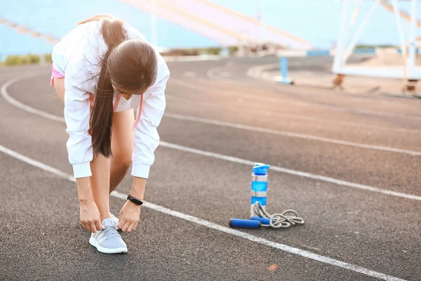 Sporty young woman tying shoelaces at the stadium — Stock Photo, Image