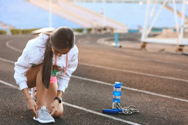 Sporty young woman tying shoelaces at the stadium — Stock Photo, Image