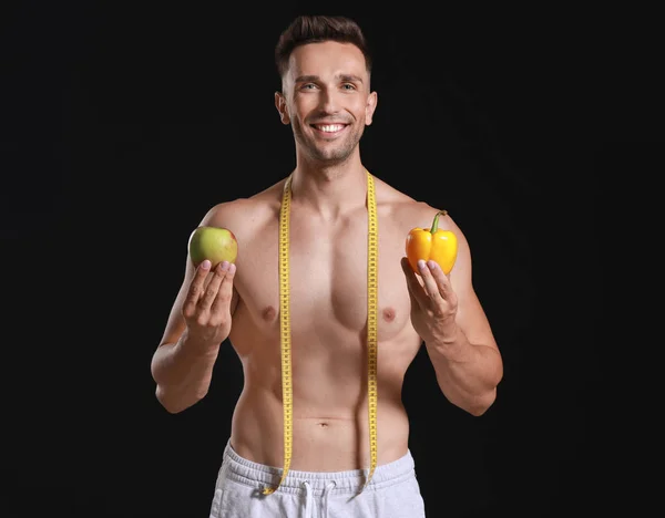 Handsome muscular man with measuring tape and food on dark background. Weight loss concept — Stock Photo, Image