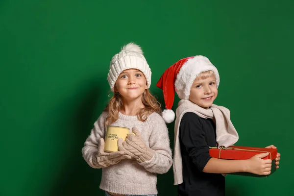 Cute little children with Christmas gift and cup of hot chocolate on color background — Stock Photo, Image