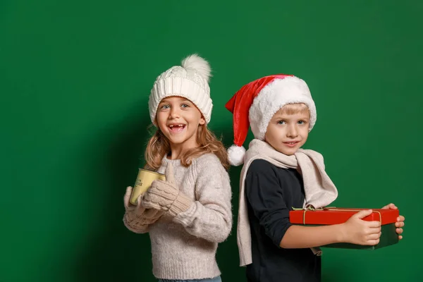 Niedliche kleine Kinder mit Weihnachtsgeschenk und Tasse heißer Schokolade auf farbigem Hintergrund — Stockfoto