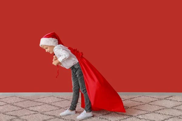 Симпатичні маленький хлопчик в капелюсі Санта Клаус і з подарунками в сумці біля кольору стіни — стокове фото