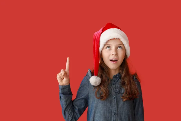 Meglepett kislány Santa Claus hat mutat valamit a színes háttér — Stock Fotó